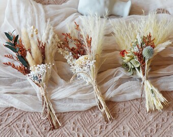 May include: Four small bouquets of dried flowers in shades of brown, white, and orange. The bouquets are tied with twine and arranged on a white fabric background.