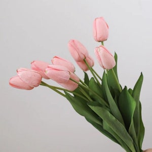 May include: A bouquet of pink artificial tulips with green stems. The tulips are arranged in a hand-held bouquet.