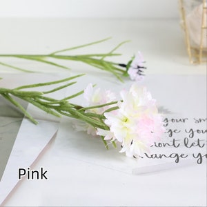 May include: A bouquet of pink and white artificial flowers with green stems. The flowers are arranged in a cluster and have a delicate, feminine appearance.