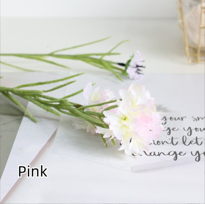 May include: A bouquet of pink and white artificial flowers with green stems. The flowers are arranged in a cluster and have a delicate, feminine appearance.