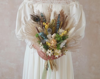 Pode incluir: Um buquê de flores secas com uma pena de pavão, capim-dos-pampas e outras flores secas em tons de bege, marrom, azul e amarelo.