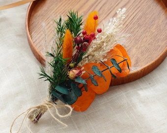 May include: A small bouquet of dried flowers with orange, red, and white accents. The bouquet is tied with twine and features dried eucalyptus leaves.
