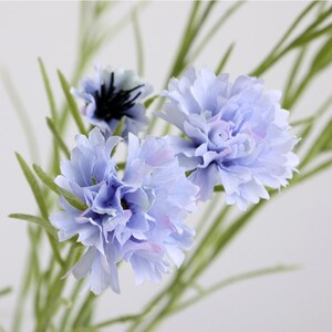 May include: A bouquet of artificial blue flowers with green stems. The flowers have a delicate, ruffled texture.