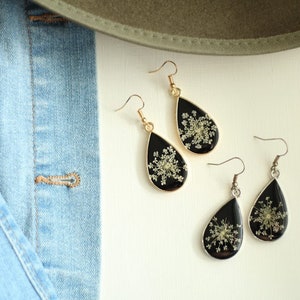 May include: Three pairs of teardrop-shaped earrings with black resin and dried white flowers. The earrings have gold-toned hooks.