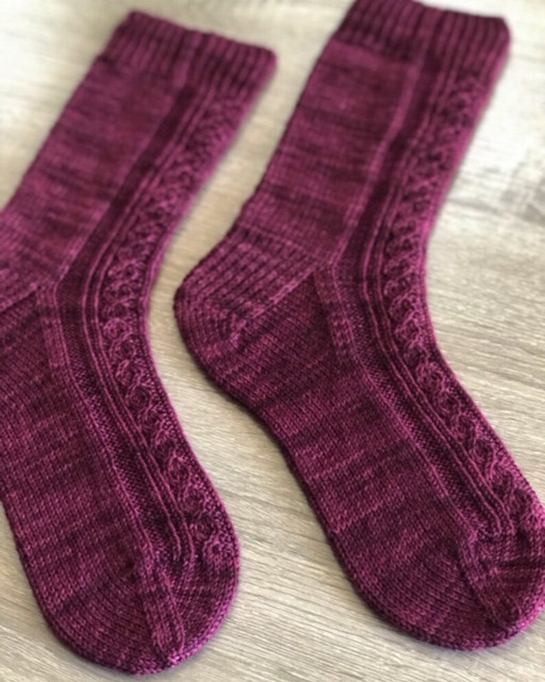 May include: A pair of knitted socks in a deep burgundy colour with a cable knit pattern. The socks are made with a soft, textured yarn.