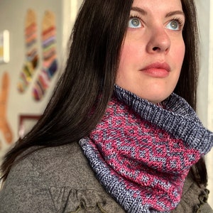 Puede incluir: Un cuello tejido en tonos rosa, blanco y azul marino. El cuello presenta un patrón texturizado y un borde azul marino acanalado. La persona de la imagen lleva un jersey gris.