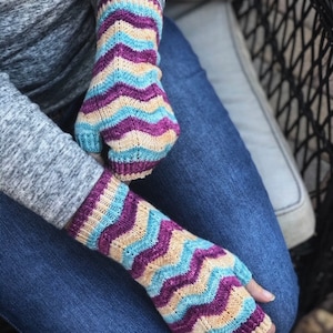 Könnte beinhalten: Ein Paar gestrickte Fingerhandschuhe mit einem Zickzackmuster in Blautönen, Lila und Beige.