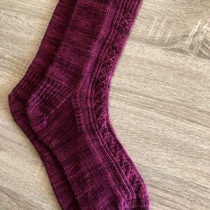 May include: A pair of knitted socks in a deep burgundy colour with a cable knit pattern. The socks are made with a fine yarn and have a soft, comfortable feel.