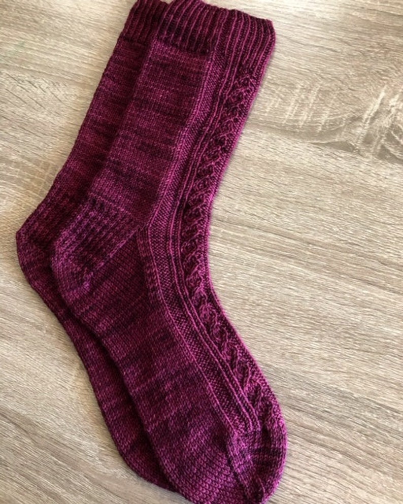 May include: A pair of knitted socks in a deep burgundy colour with a cable knit pattern. The socks are made with a fine yarn and have a soft, comfortable feel.