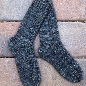 May include: A pair of hand-knitted socks in shades of gray and teal. The socks feature a textured cable knit pattern and ribbed cuffs. The yarn has a speckled appearance, adding visual interest to the cozy, warm socks.