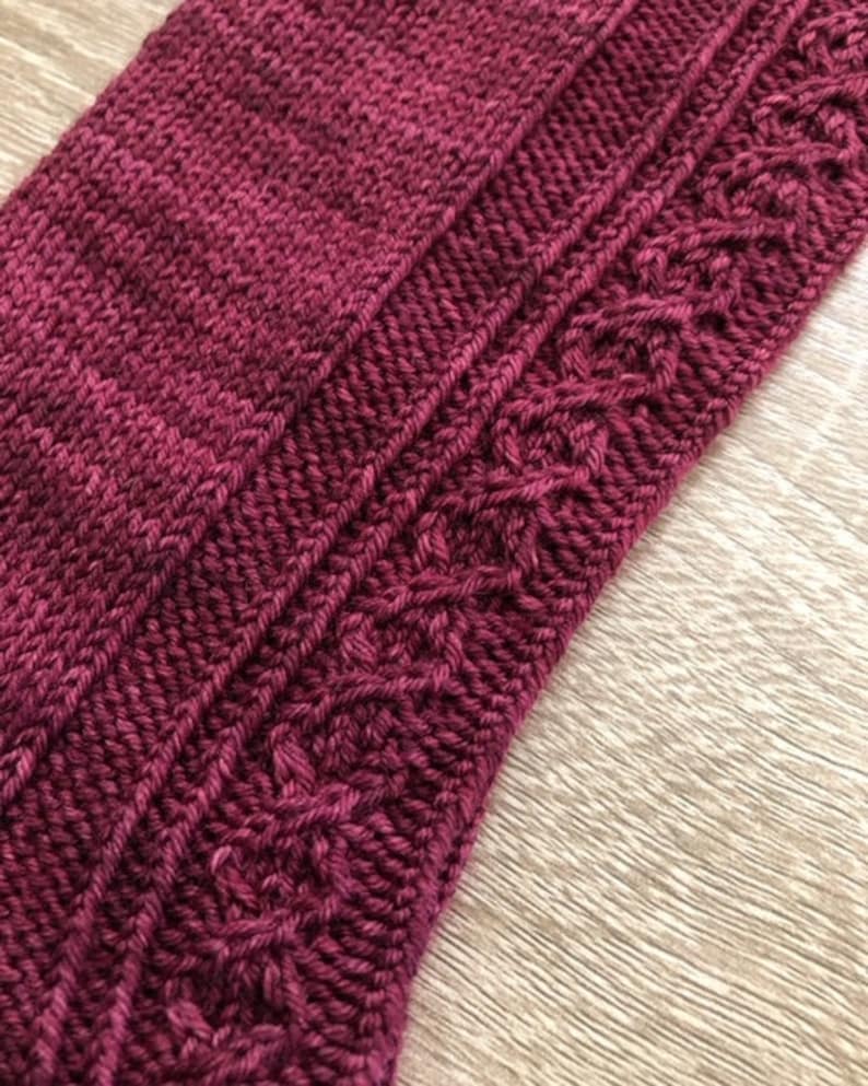 May include: Close-up of a knitted fabric with a cable pattern. The fabric is a deep burgundy colour.
