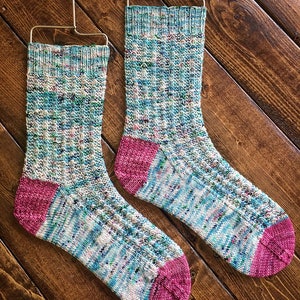 May include: A pair of hand-knitted socks in a blue, green, and white speckled yarn with pink heels and toes.