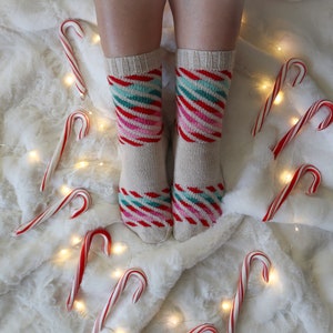 May include: A pair of white socks with red, green, and blue stripes. The socks are on a white fuzzy surface with red and white candy canes scattered around.
