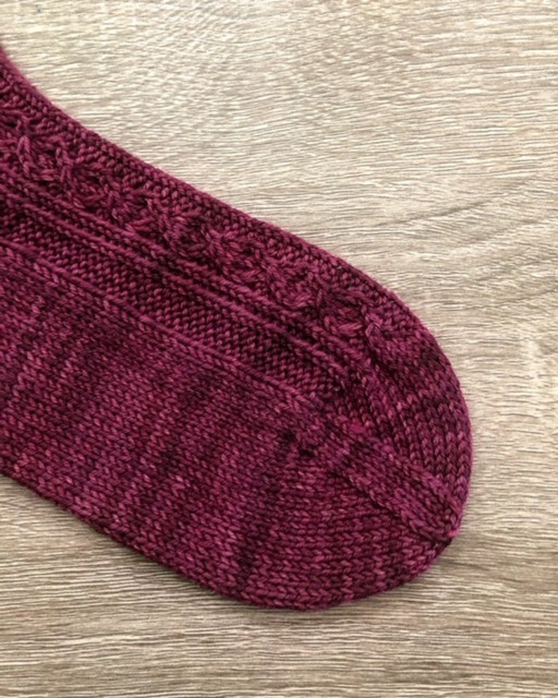 May include: Close-up of a burgundy knitted sock with a cable pattern.