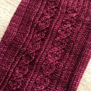 May include: Close-up of a deep burgundy knitted fabric with a cable knit pattern.