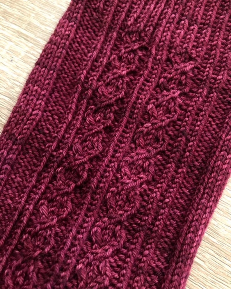 May include: Close-up of a deep burgundy knitted fabric with a cable knit pattern.