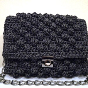 May include: A black crocheted clutch bag with a silver chain strap and a silver clasp.
