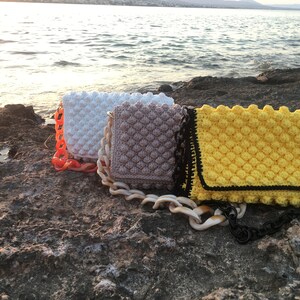 May include: Three crocheted handbags with bubble texture in white, beige, and yellow with black trim. Each bag has a chunky plastic chain strap.