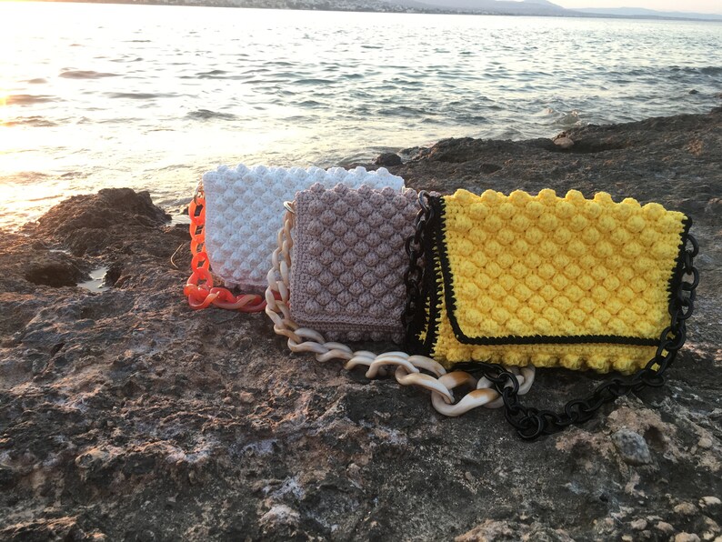 May include: Three crocheted handbags with bubble texture in white, beige, and yellow with black trim. Each bag has a chunky plastic chain strap.