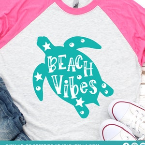 May include: A teal blue sea turtle silhouette with white stars and the text "BEACH Vibes" in white lettering on a gray and pink t-shirt.