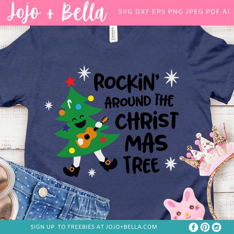 Puede incluir: Una camiseta azul con un &aacute;rbol de Navidad de dibujos animados tocando la guitarra. El texto "Rockin' Around The Christ Mas Tree" est&aacute; impreso en la camiseta.