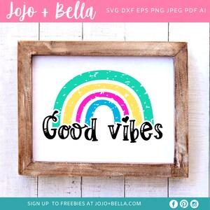 Op de afbeelding: Een ingelijst afdruk met een regenboogontwerp en de tekst "Good vibes" in zwarte letters. De regenboog is gemaakt van vijf kleuren: groen, geel, roze, blauw en wit. De achtergrond is wit.