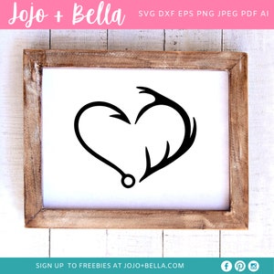 May include: A black and white silhouette of a heart formed by a fishing hook and an antler. The image is on a white background within a wooden frame.