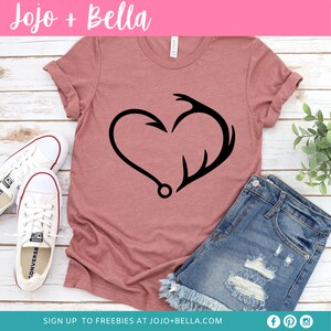 May include: A pink t-shirt with a black graphic of a heart made from a fishing hook and an antler. The text "Jojo + Bella" is at the top of the image.