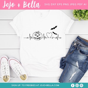 May include: A white t-shirt featuring a black graphic of a pumpkin, a heart, and bats with a heartbeat line. The text "Jojo + Bella" is at the top of the image.