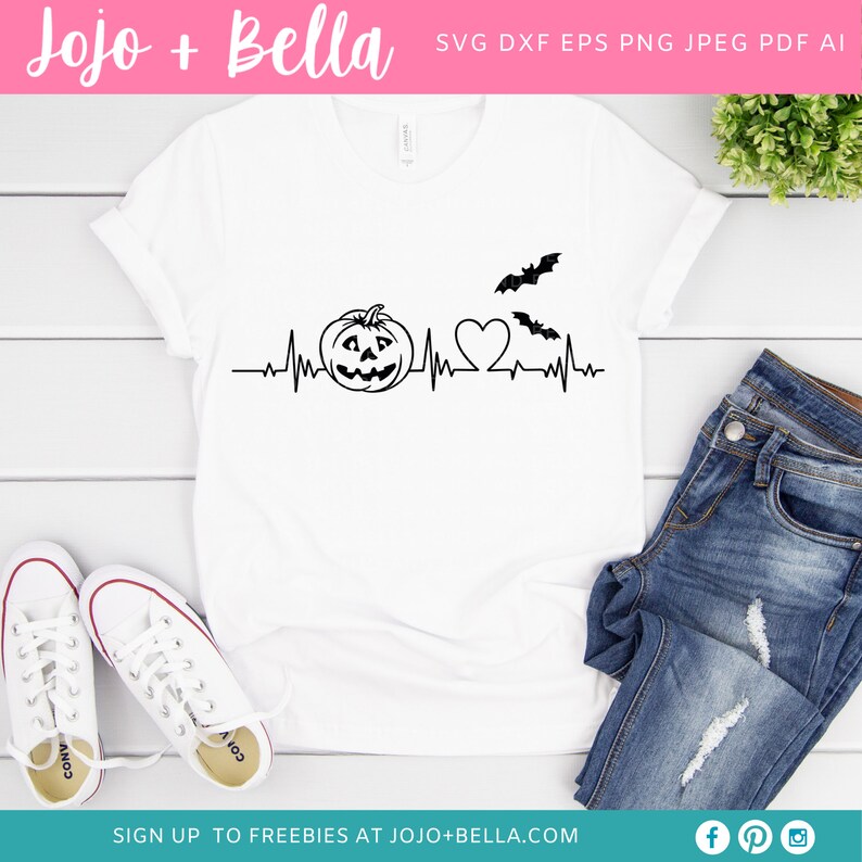 May include: A white t-shirt featuring a black graphic of a pumpkin, a heart, and bats with a heartbeat line. The text "Jojo + Bella" is at the top of the image.