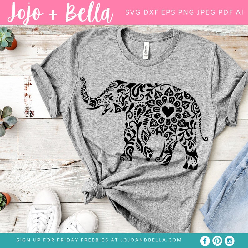 Peut inclure: Un t-shirt gris avec un motif d'&eacute;l&eacute;phant mandala noir. L'&eacute;l&eacute;phant a un c&oelig;ur au centre de son mandala. Le t-shirt est pos&eacute; sur une surface en bois avec des baskets blanches et un jean bleu.