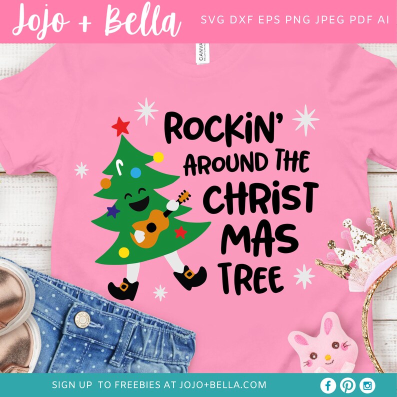 Puede incluir: Camiseta rosa con un &aacute;rbol de Navidad de dibujos animados tocando la guitarra y el texto "Rockin' Around The Christ Mas Tree".