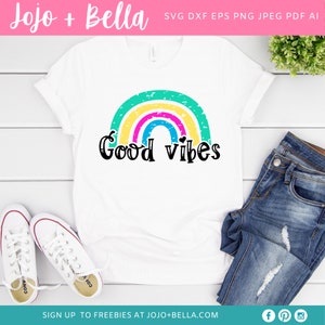 Op de afbeelding: Een wit T-shirt met een regenboogontwerp en de tekst "Good vibes" in zwart. De regenboog is gemaakt van groene, gele, roze en blauwe strepen met een verweerde look.