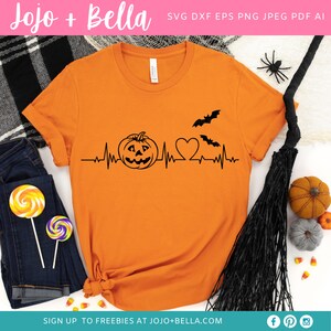 May include: Orange t-shirt with a black graphic of a pumpkin, heart, and bats with a heartbeat line. The text "SIGN UP TO FREEBIES AT JOJO+BELLA.COM" is at the bottom of the shirt.