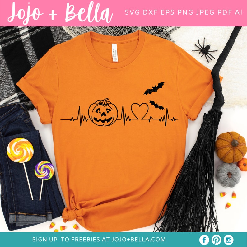 May include: Orange t-shirt with a black graphic of a pumpkin, heart, and bats with a heartbeat line. The text "SIGN UP TO FREEBIES AT JOJO+BELLA.COM" is at the bottom of the shirt.