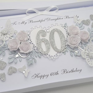May include: A white birthday card with a decorative design. The card features a silver glitter "60" in the center, surrounded by paper flowers, butterflies, and hearts. The text "Happy 60th Birthday" is written at the bottom.