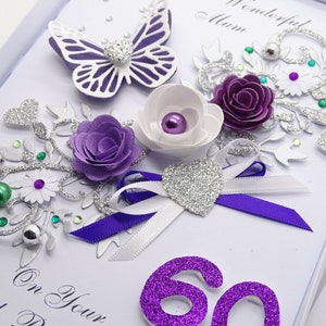 May include: A handmade card with a purple and silver design. The card features a butterfly, flowers, and a ribbon. The number 60 is written in purple glitter. The text "On Your 60th Day" is written in black ink.