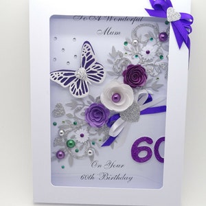 May include: A handmade card with a white background and a purple butterfly, flowers, and glitter. The card says "To A Wonderful Mum" and "On Your 60th Birthday".