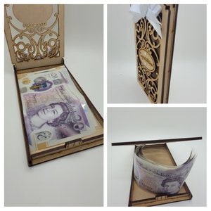 May include: A wooden money box with an open lid, filled with twenty-pound notes. The box has an ornate, laser-cut design on the lid and front. The words "Congratulations" are visible on the front of the box. A white bow is attached to the top.