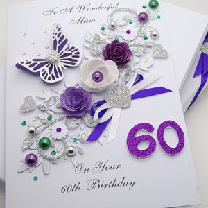 May include: A white card with a purple butterfly, flowers, and glitter. The card says "To A Wonderful Mum On Your 60th Birthday" and has the number 60 in purple glitter.