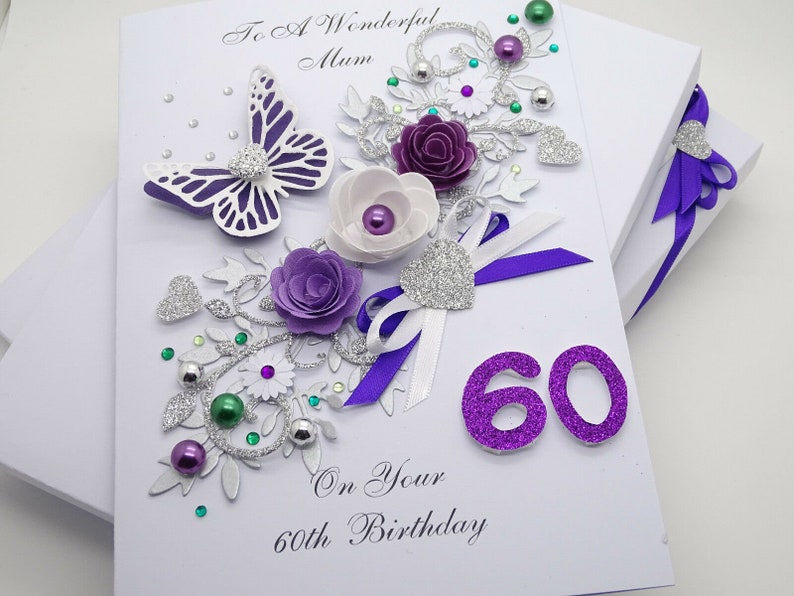 May include: A white card with a purple butterfly, flowers, and glitter. The card says "To A Wonderful Mum On Your 60th Birthday" and has the number 60 in purple glitter.