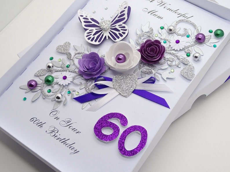 May include: A white card with a purple and silver floral design, a butterfly, and the number 60 in purple glitter. The card reads "To a Wonderful Mum" and "On Your 60th Birthday".