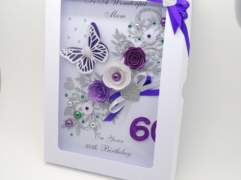 May include: A white card with a purple and silver butterfly, flowers, and glitter. The card says "To A Wonderful Mum" and "On Your 60th Birthday".