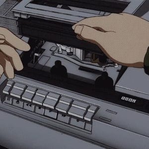 May include: An animated image of a vintage tape deck with hands interacting with the device. The tape deck is silver with black accents and buttons. The hands are tan and appear to be opening the tape deck.