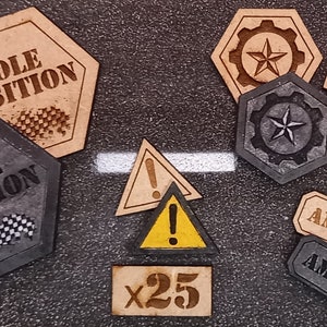 Könnte beinhalten: Ein Satz hölzerner Spielsteine für ein Brettspiel. Die Steine sind in Form von Sechsecken, Quadraten und Dreiecken. Die Steine sind in Braun und Schwarz bemalt. Die Steine haben Text darauf, darunter "Pole Position", "Ammo", "x1", "x10" und "x25".