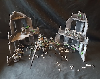 May include: A black and green spider-like robot with glowing green weapons stands in a ruined cityscape.  The robot is surrounded by smaller, black and green figures with glowing green weapons.  The figures are standing on platforms made of gray cardboard.