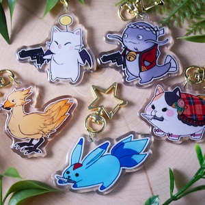 May include: A collection of acrylic keychains featuring cartoon characters. The keychains depict a white cat with a gun, a yellow bird with a knife, a blue rabbit with a knife, a gray fish-like creature, and a calico cat with a knife. Each keychain has a gold-colored clasp.