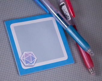 Op de afbeelding: Een blauwe vierkante plakbriefje met een witte rand en een paars en blauw geometrisch ontwerp in de linkerbenedenhoek. Twee pennen, een blauwe en een rode, liggen op het plakbriefje.