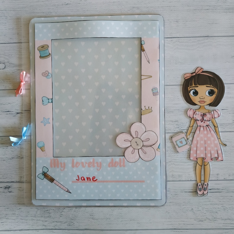 May include: A light blue and pink scrapbook page with a blank photo frame, a pink flower, and the text "My lovely doll Jane".