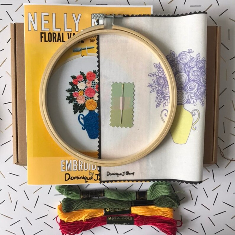 May include: Embroidery kit with a wooden hoop, fabric, and embroidery floss. The fabric has two designs, one with a blue vase and flowers and the other with a yellow vase and flowers. The kit includes the text "Embroid by Dominique J."